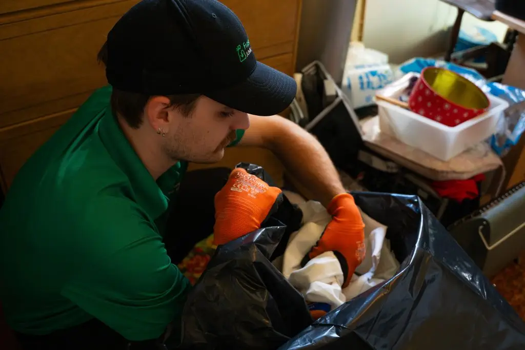 A FVJS team member loading some garbage into a trash bag with orange gloves and a company uniform