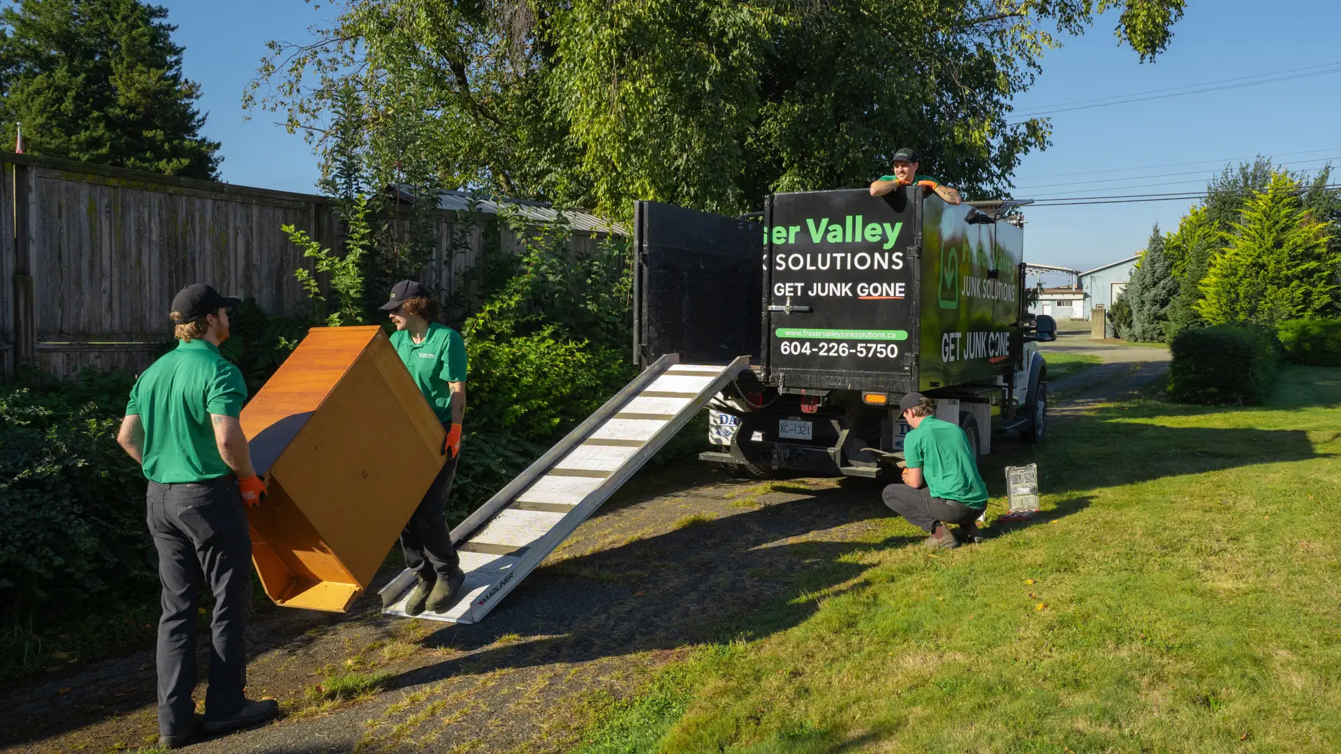 Two Fraser Valley Junk Solutions employees loading up a truck using a designated ramp while two other employees work on loading up other items in Chilliwack with blue skies.