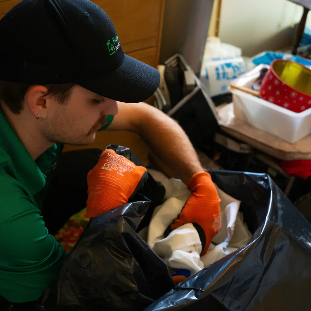 A Fraser Valley Junk Solutions employee bagging a bunch of loose debris on the floor of a bedroom in a Chilliwack house.